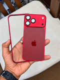 A hand holds a red iPhone case with a matching red back plate and clear outer bumper over an iPhone, with a beige upholstered chair and wooden chair legs in the background.