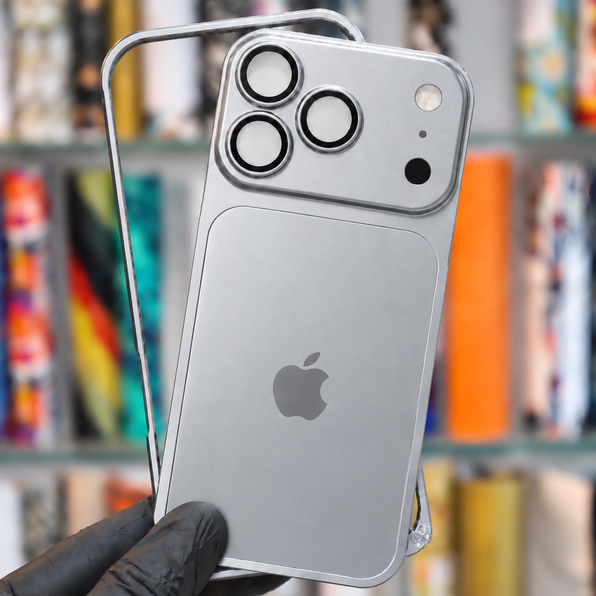 A silver smartphone case with a built-in magnetic card reader, shown fitted on a phone held by a gloved hand. The background is a blurred bookshelf.