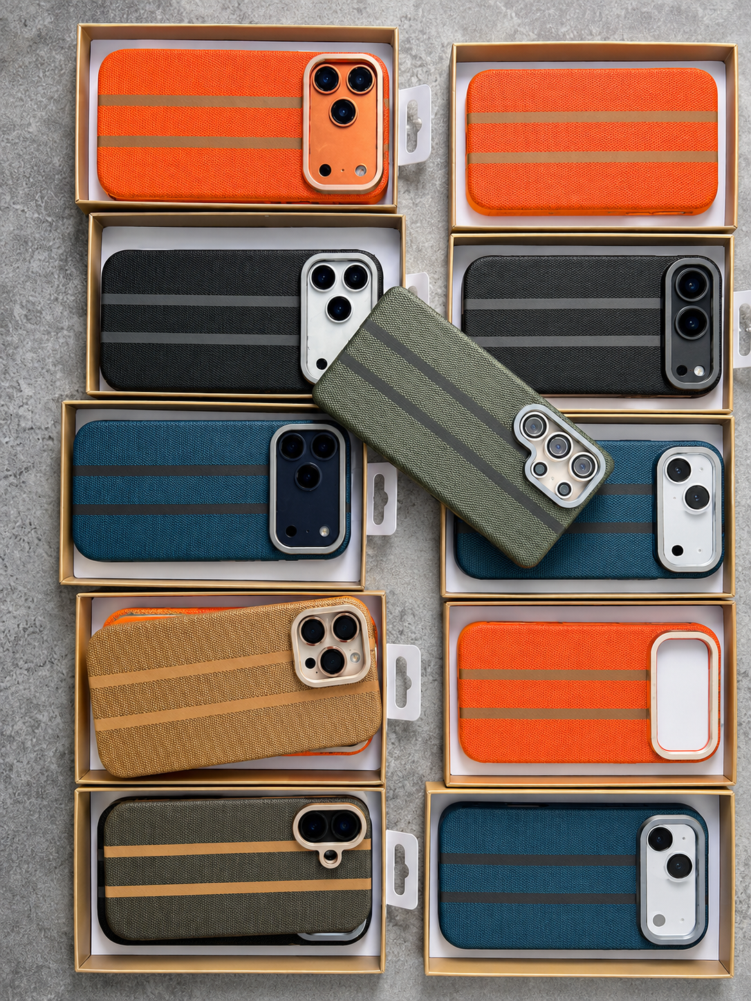 A collection of striped phone cases in various colors (orange, black, blue, green, brown) displayed inside their wooden packaging boxes on a gray textured surface, with one green case placed diagonally on top.